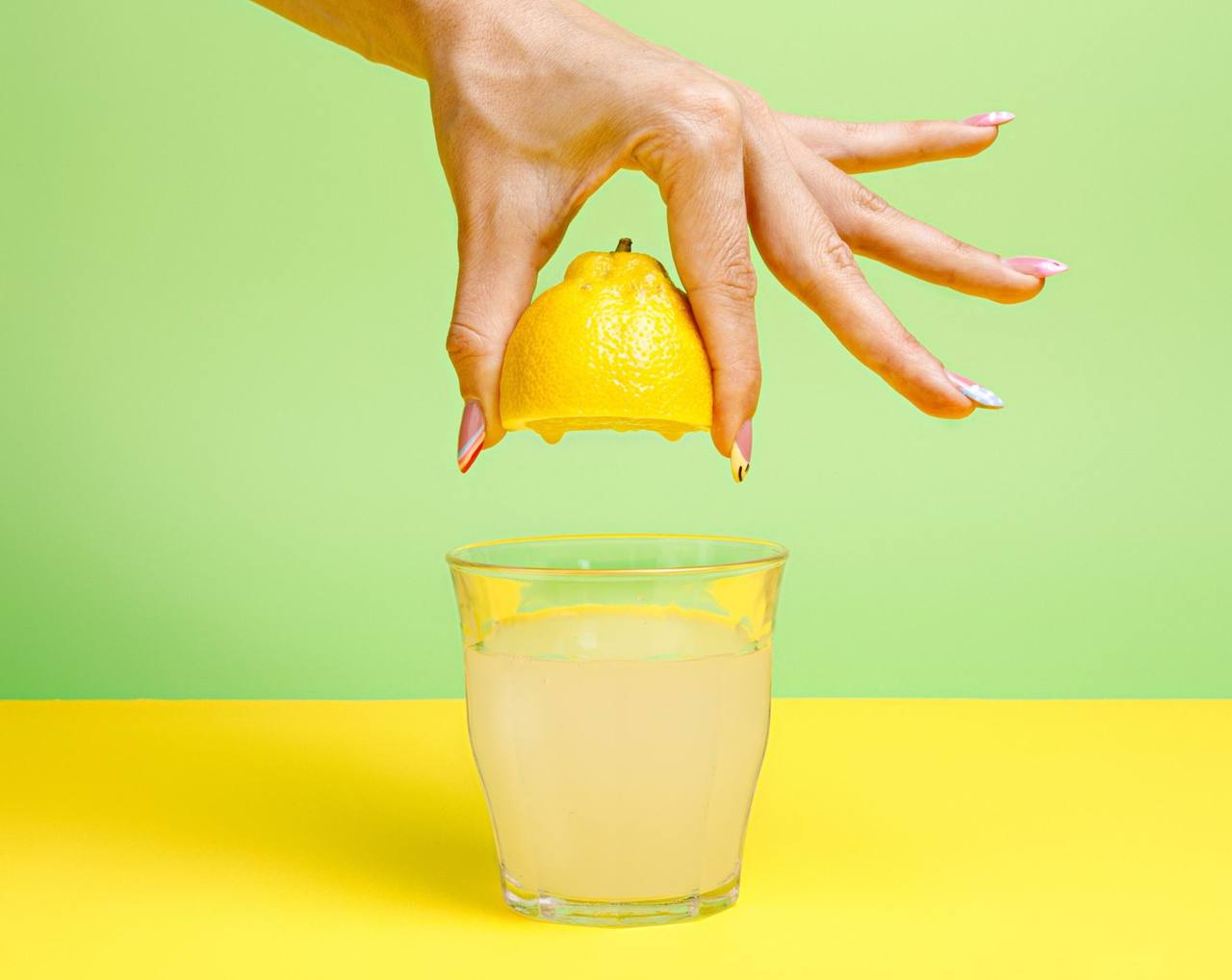 Main pressant un demi-citron au-dessus d’un verre de limonade